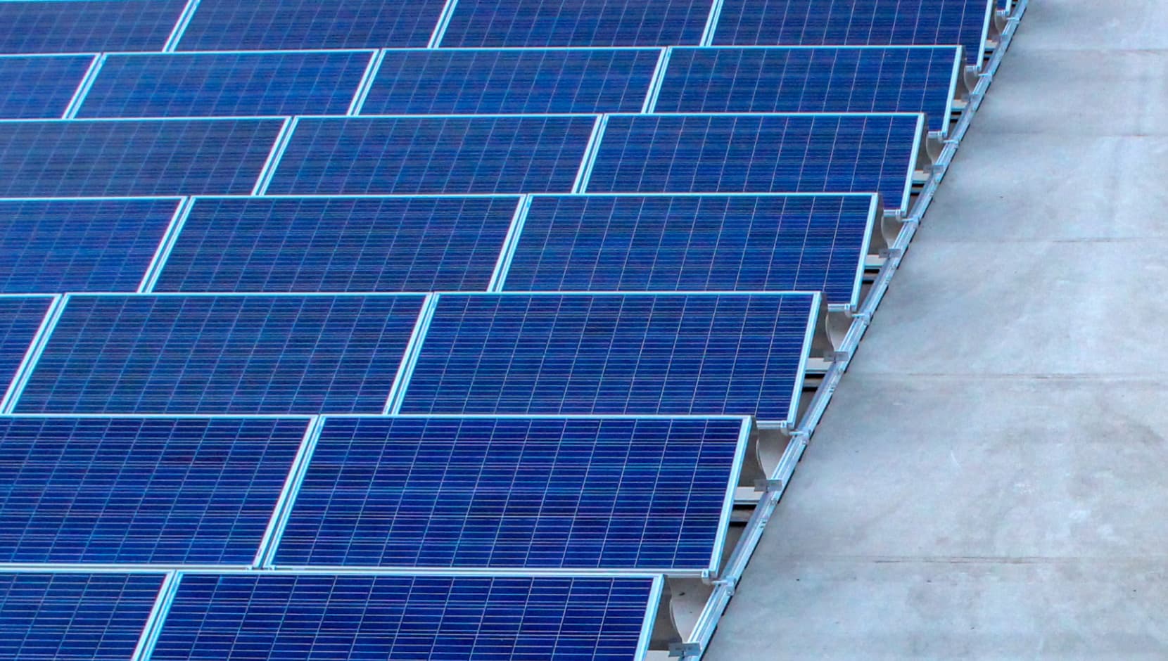 A large array of blue solar panels installed on a concrete surface, arranged in neat rows.